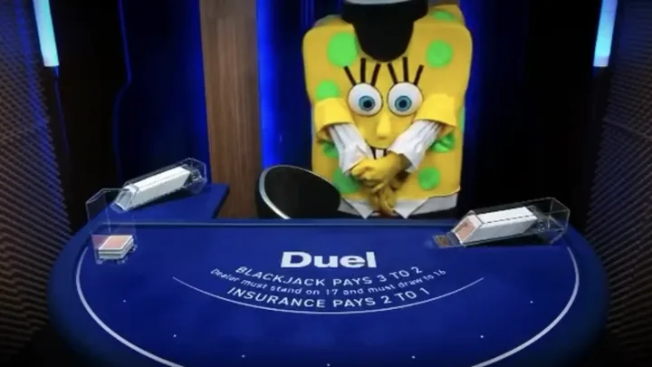 A yellow costume with green spots and oversized eyes standing at the dealer position of the Duel Blackjack table