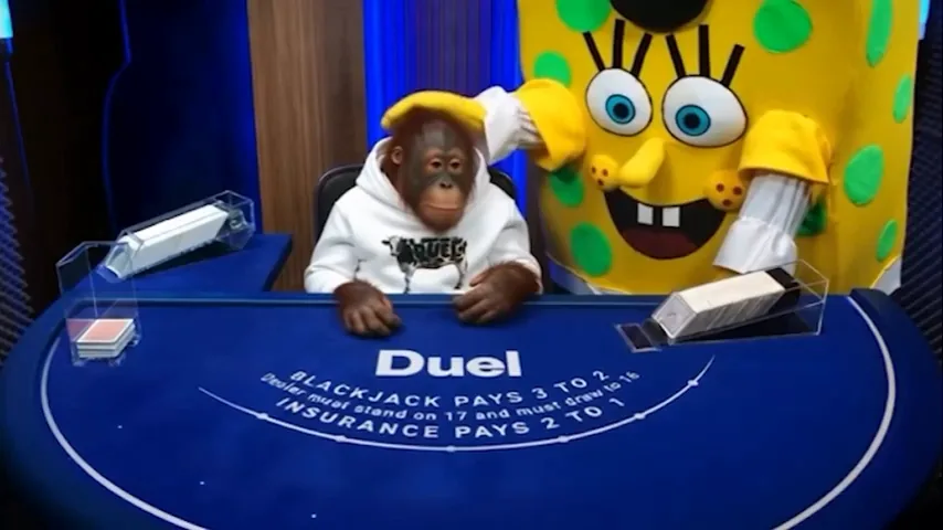 A yellow spotted costume standing behind an orangutan in the dealer chair at the Duel Blackjack table